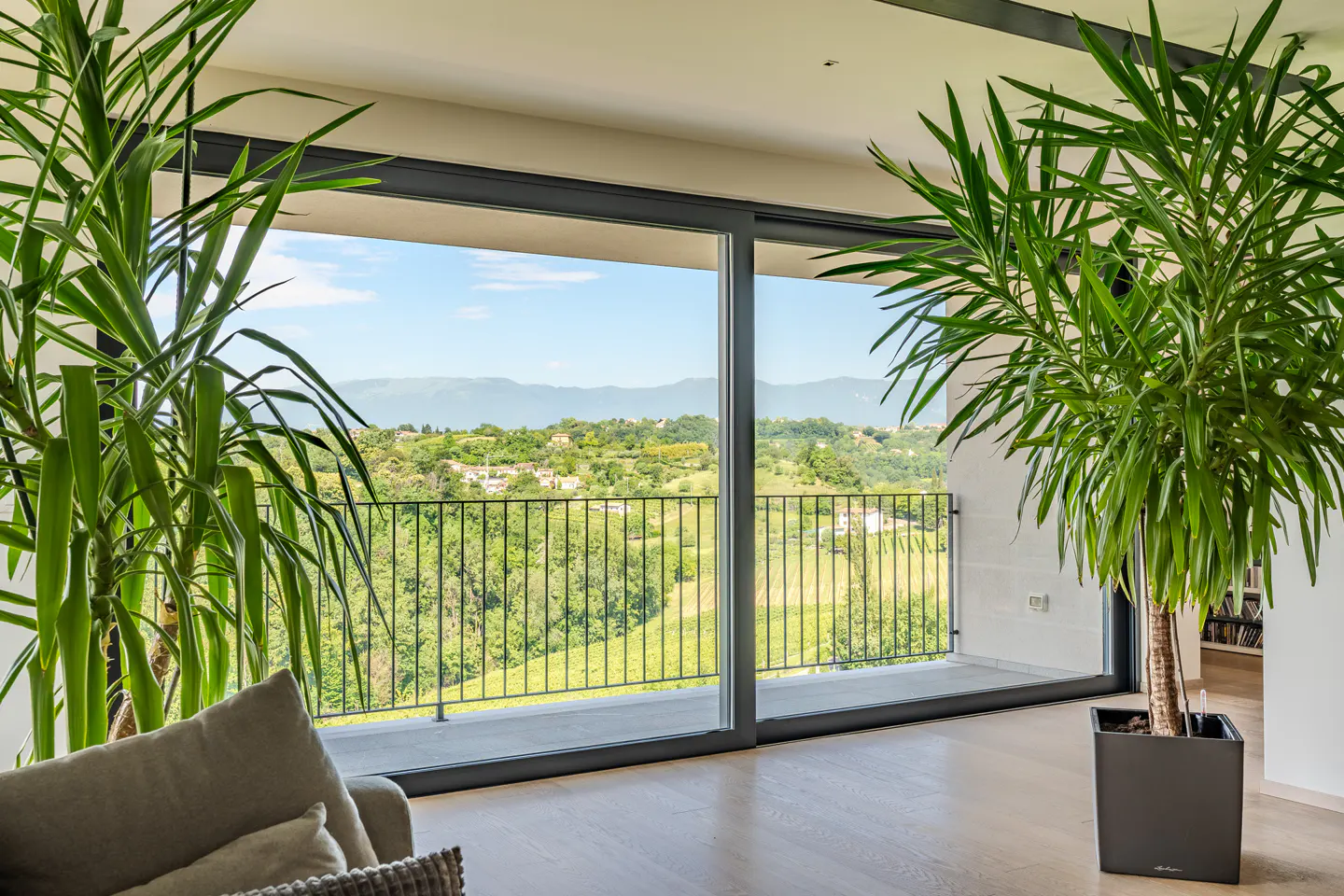 Modern living room with large sliding glass doors opening to a balcony overlooking a scenic green valley and mountains.
