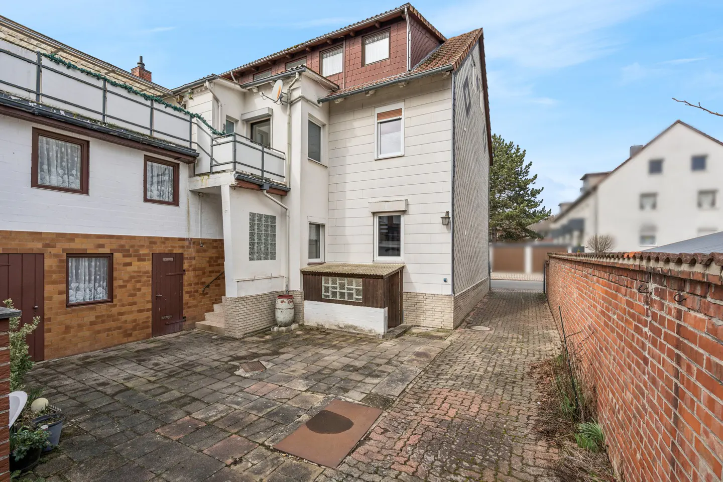 Exterior view of a white two-story house with a brick patio and a brick wall on the right.