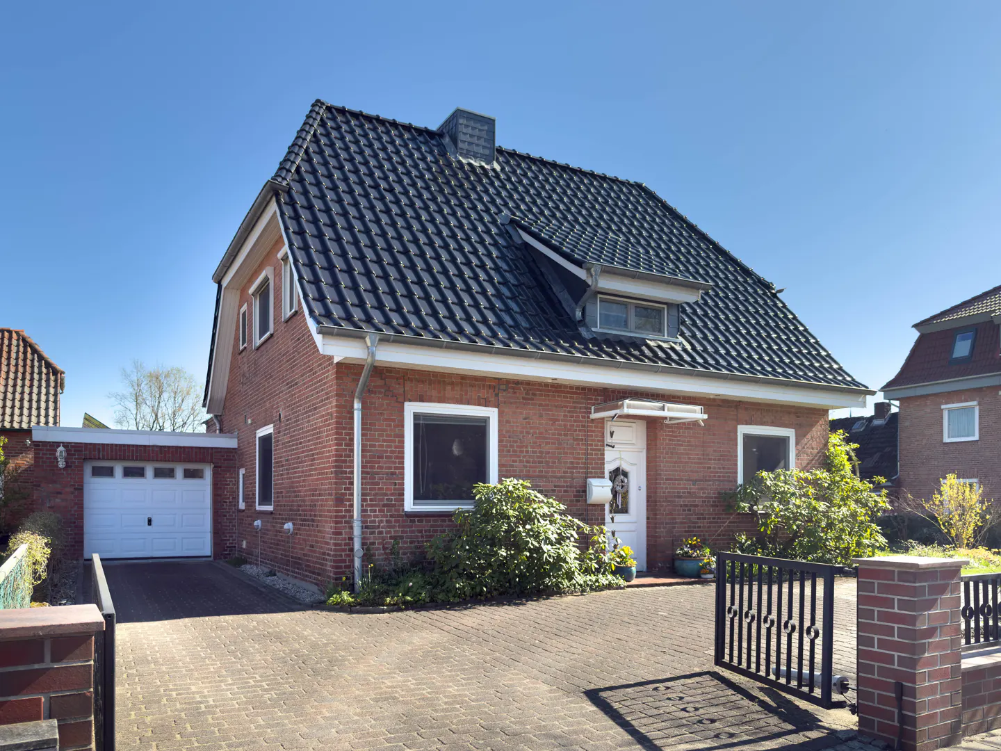Red brick house with a dark roof, white trim, and a brick driveway under a clear blue sky.