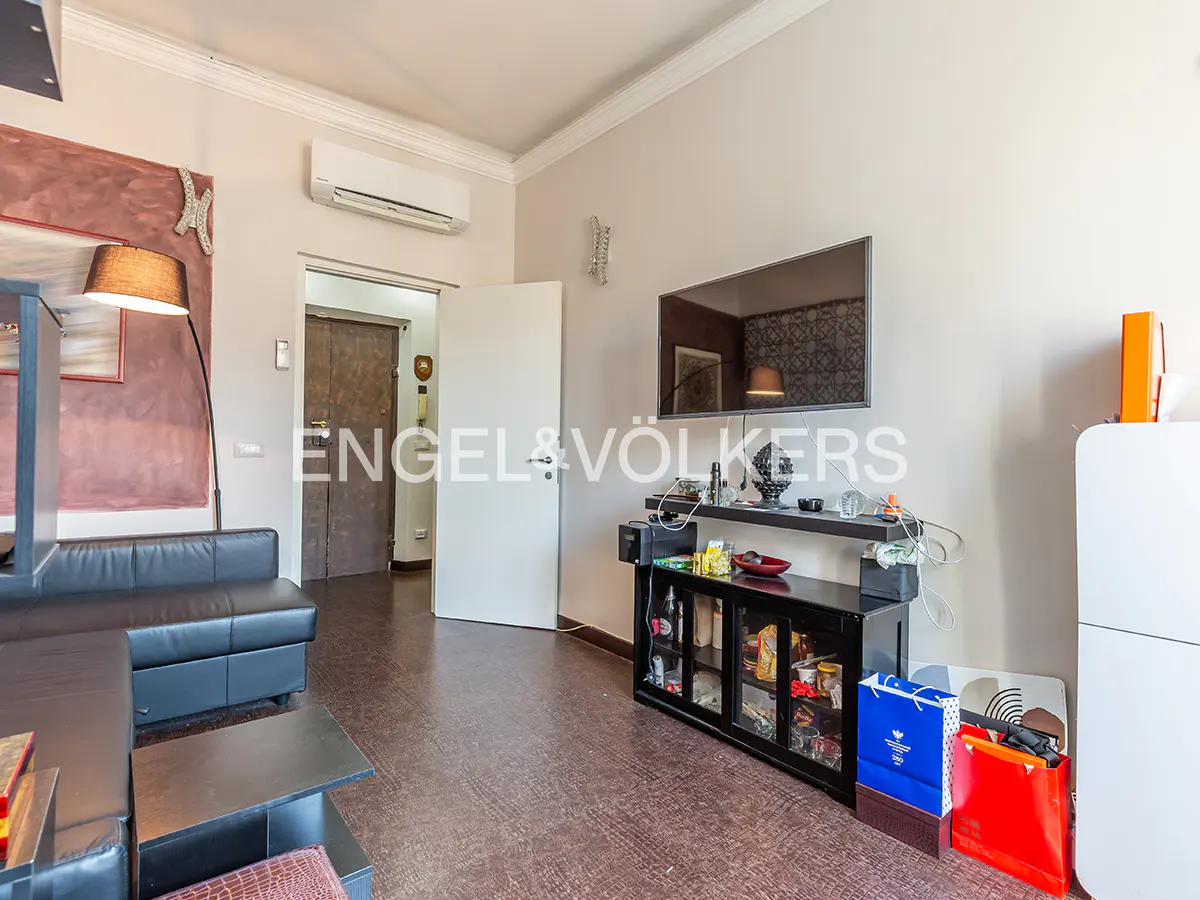 Living room with black leather sofa, TV, black cabinet, and shopping bags on a brown floor.