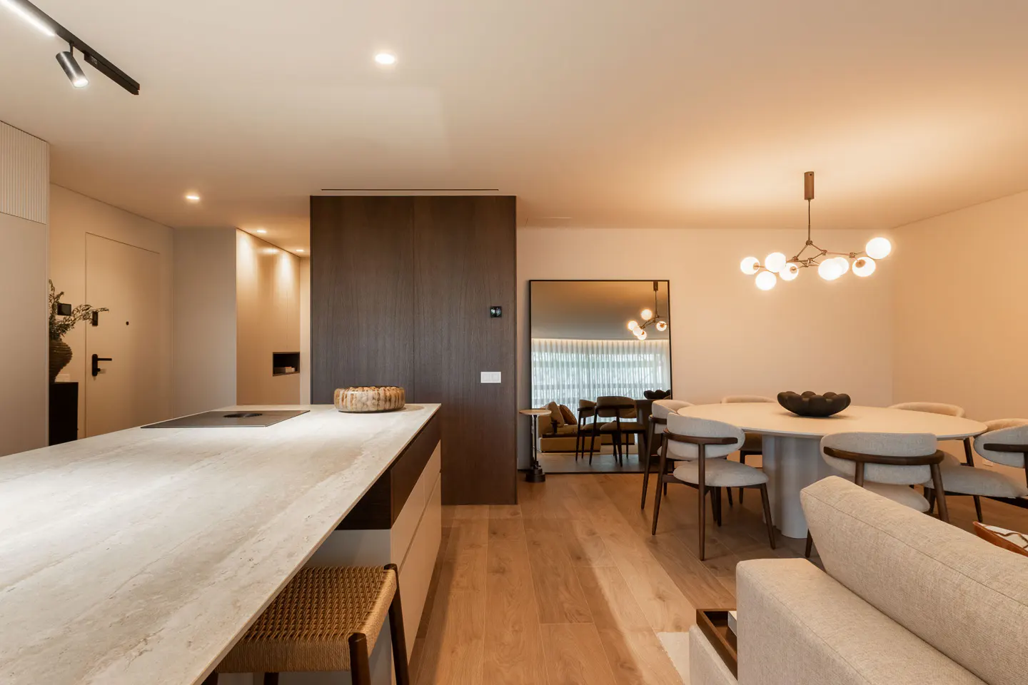 Modern open-plan kitchen and dining area with a stone island, round table, and warm wood flooring.