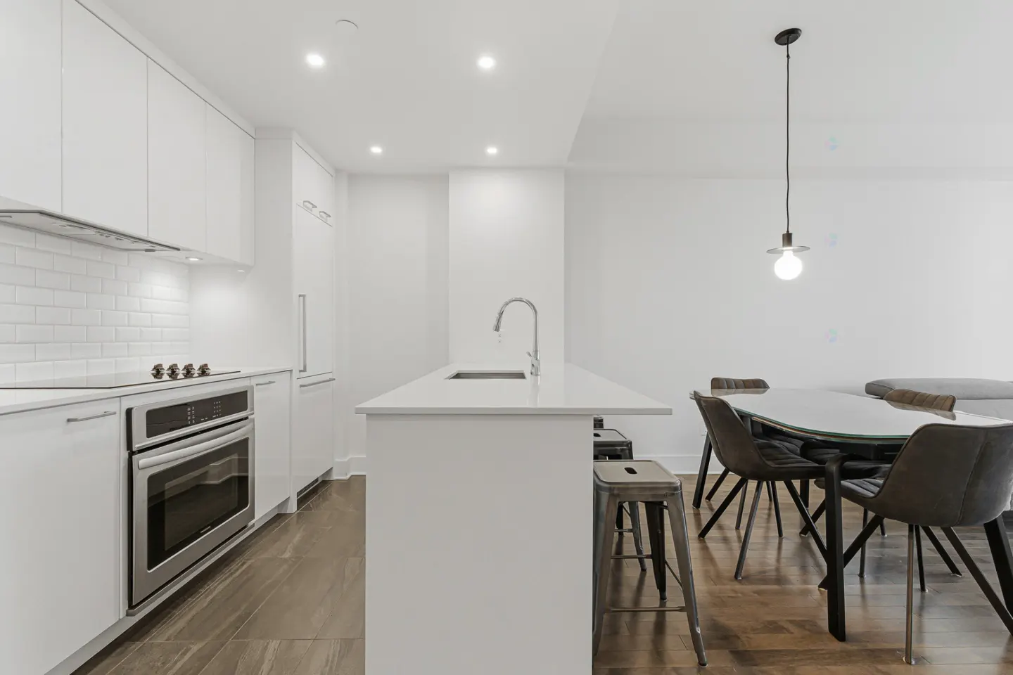 Bright, modern kitchen with white cabinets, stainless steel appliances, and a central island. A round glass table with chairs is visible in the background.