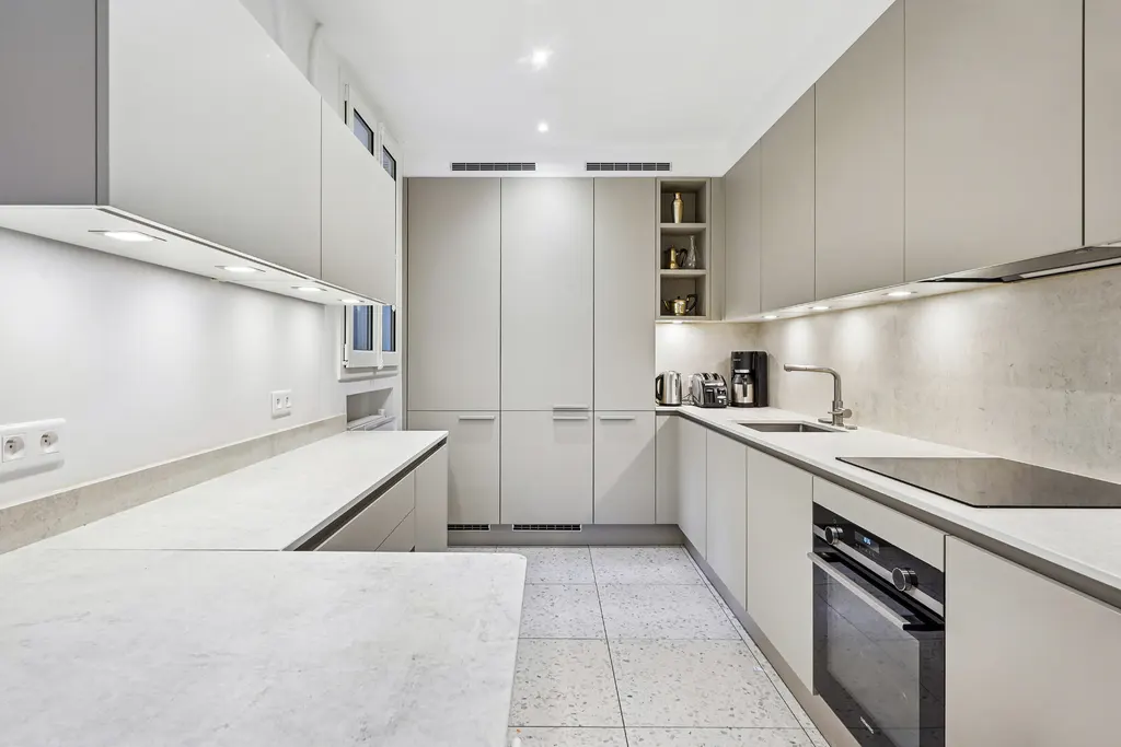 Bright, modern kitchen with light gray cabinets, stone countertops, and stainless steel appliances. Recessed lighting illuminates the space.