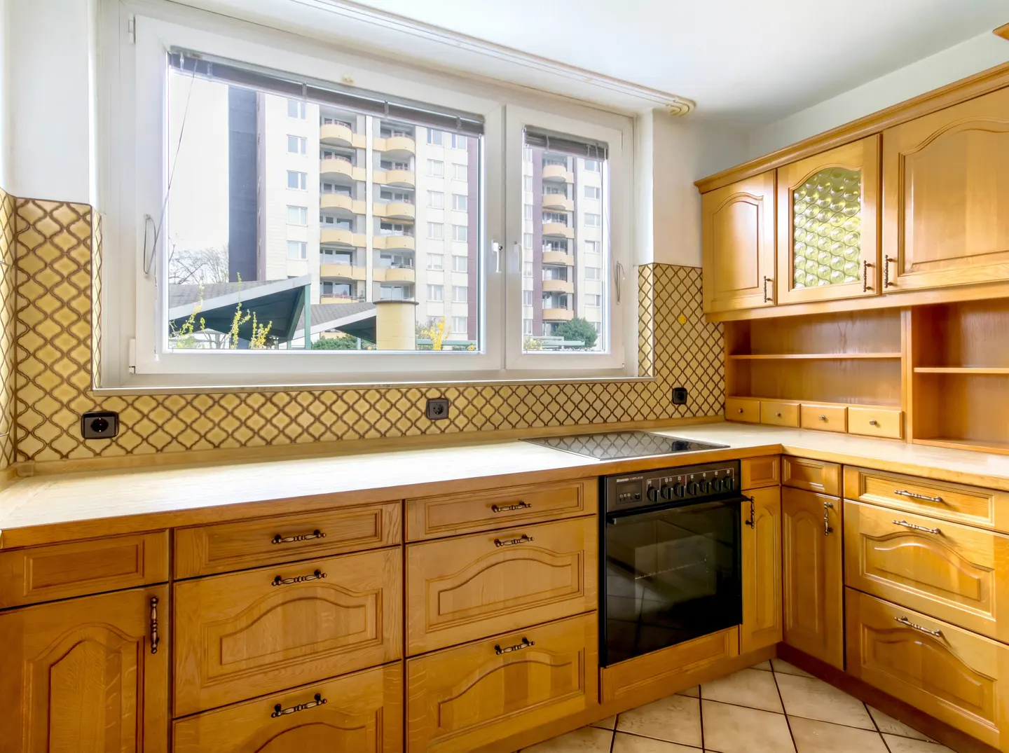 A kitchen with light wood cabinets, a black oven, and a window overlooking a building.
