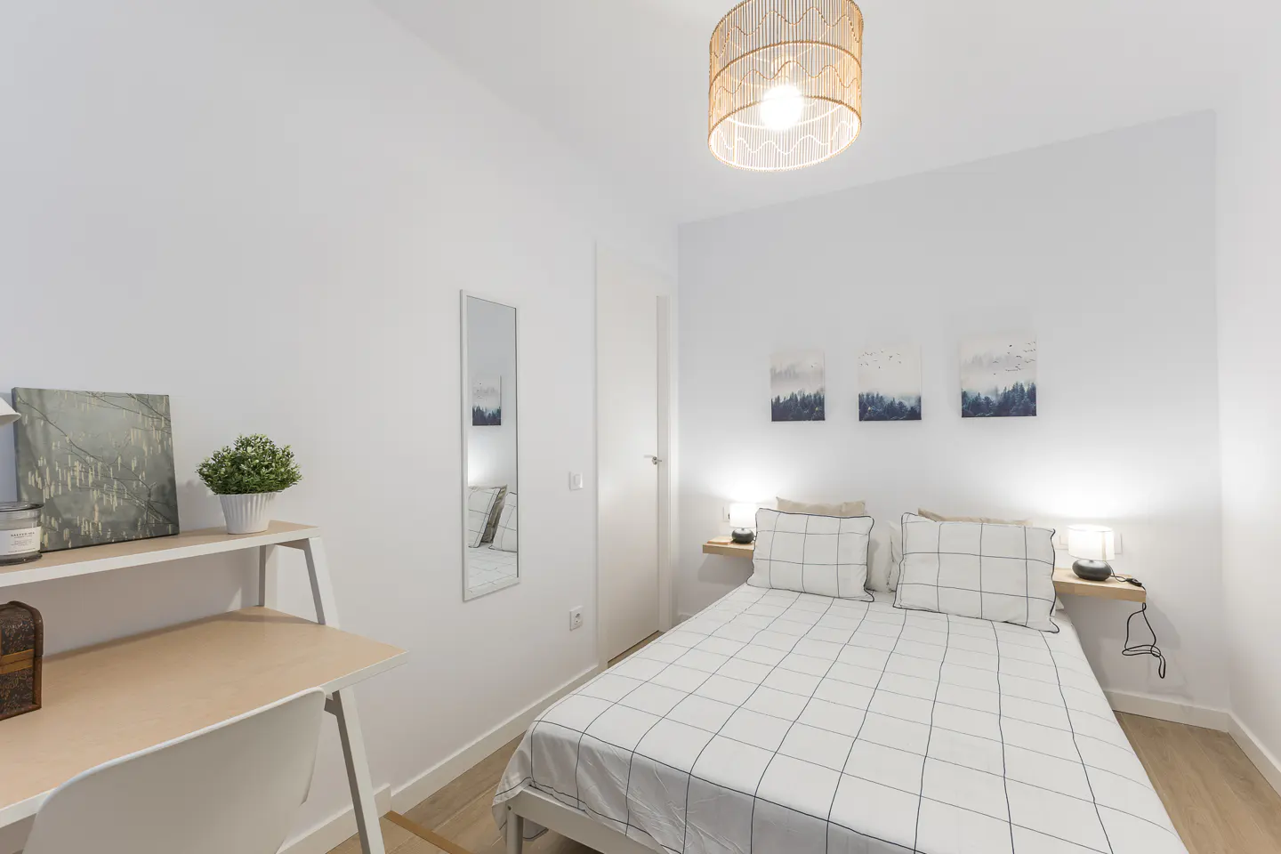 Bright bedroom with white walls, a bed with a grid pattern, a desk, and a woven pendant light.