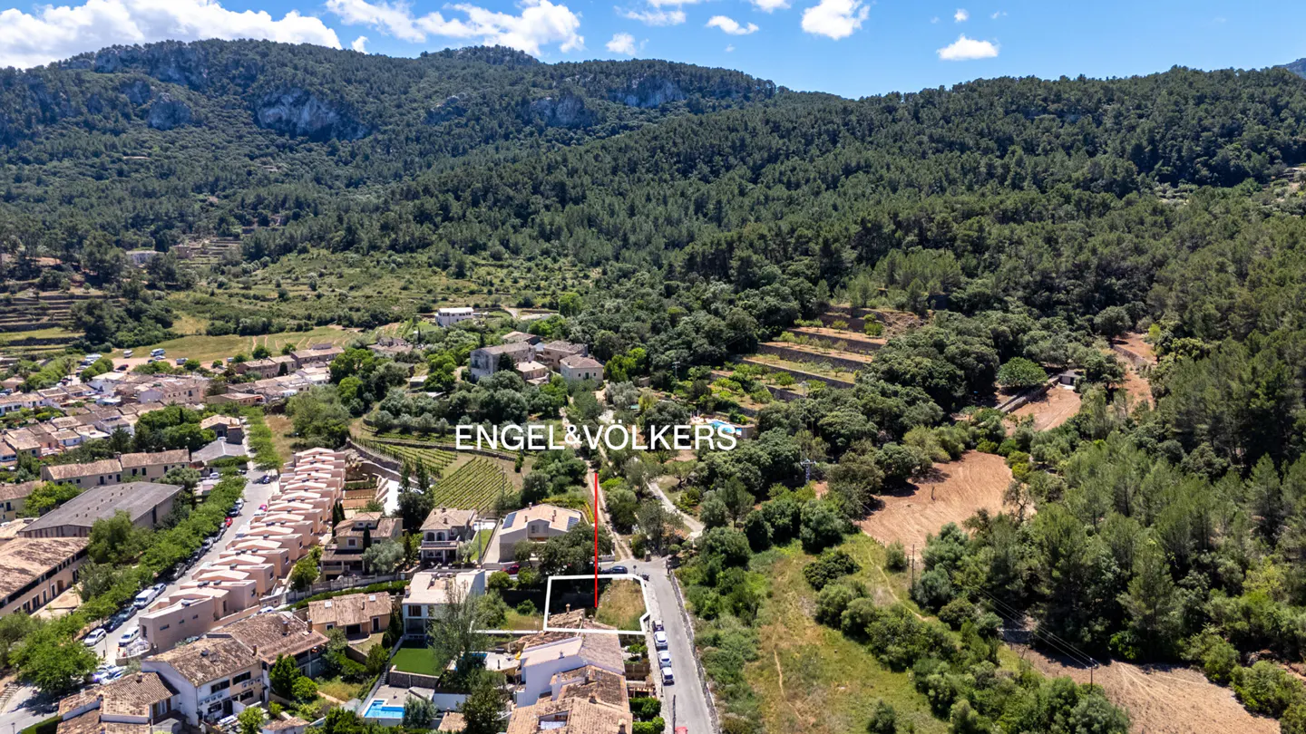 Aerial view of a property lot in a village with mountains and trees in the background.