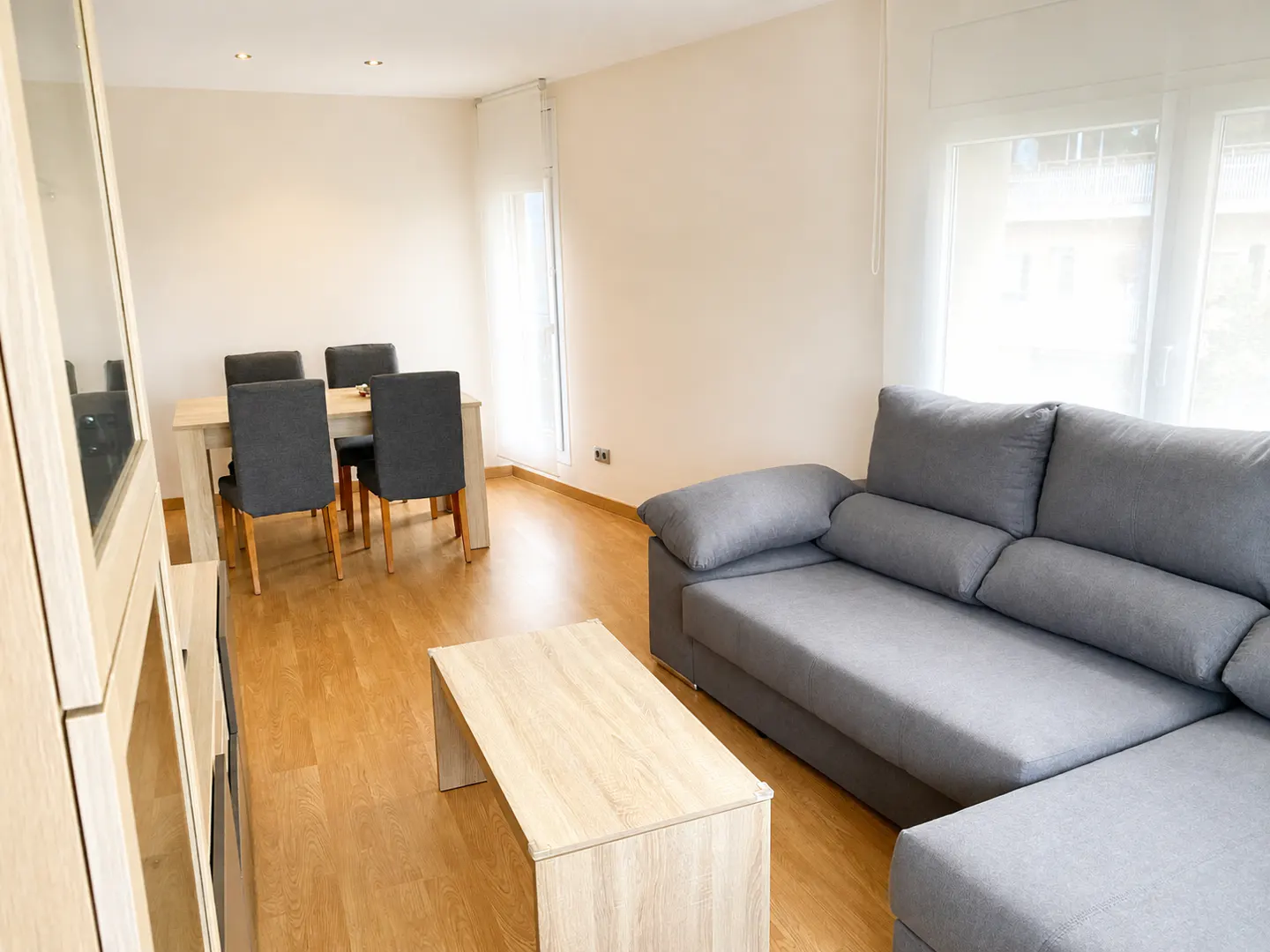 Living room with gray sofa, wood coffee table, dining table with four chairs, and wood floor.