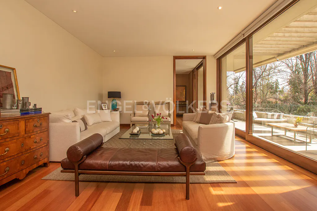 Living room with hardwood floors, white sofas, leather bench, glass table, and large windows to a patio.