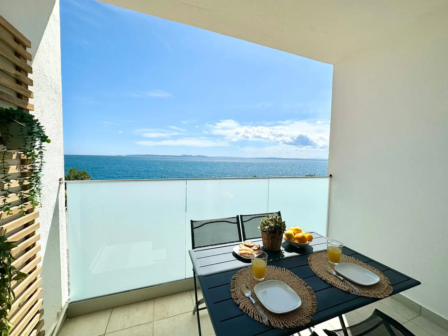 Balcony with a table set for breakfast overlooking the ocean on a sunny day.