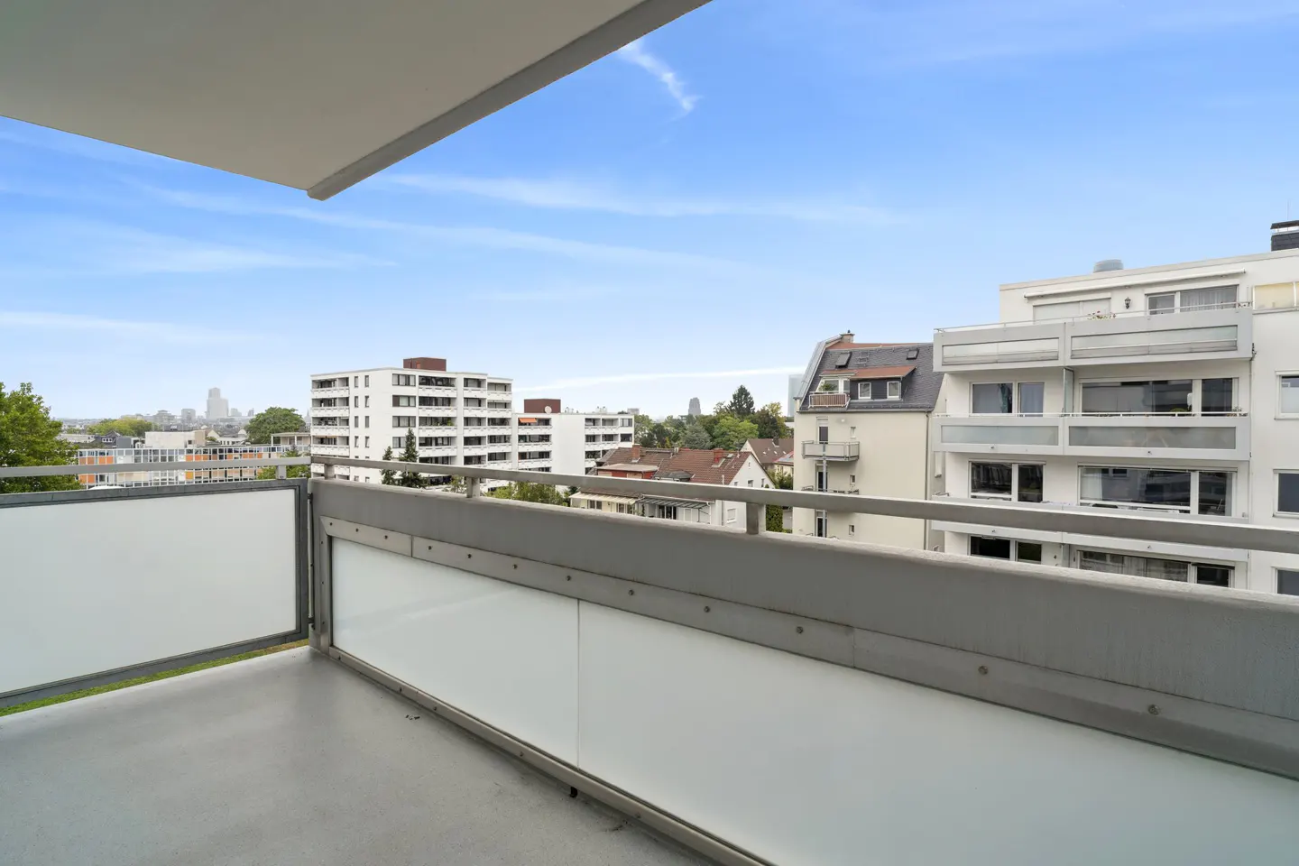 View from a balcony with a gray railing, overlooking white buildings and a blue sky.