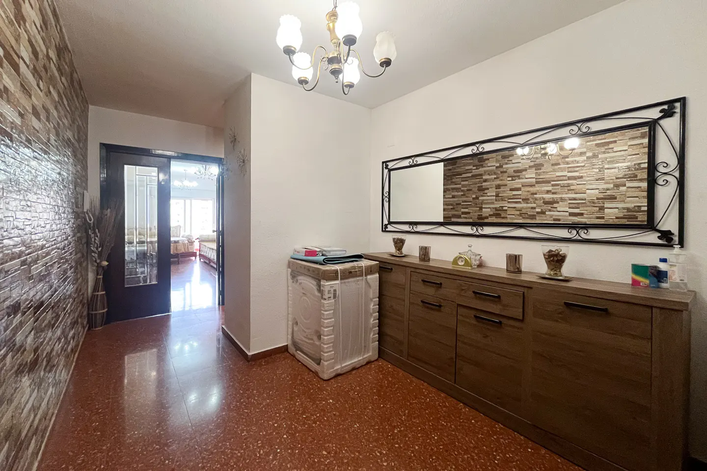 A home's entryway with a brick accent wall, a wooden cabinet with a mirror, and a chandelier.
