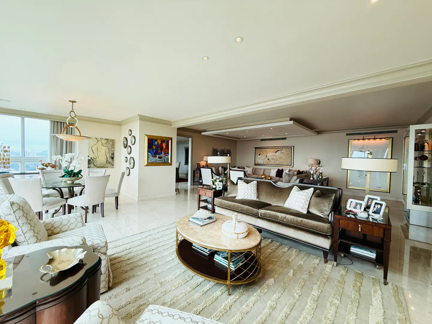 A spacious living room with a dining area, featuring a brown sofa, oval coffee table, and marble floors.