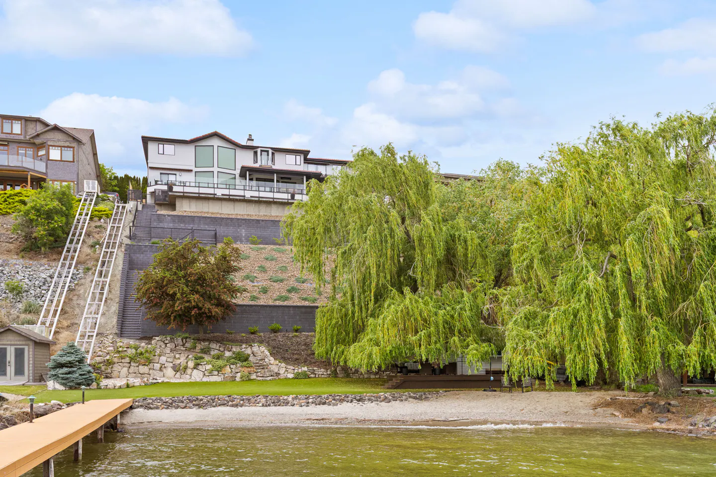 Lakefront home with a private dock and a tram to the house on a hill. A large willow tree is on the right.