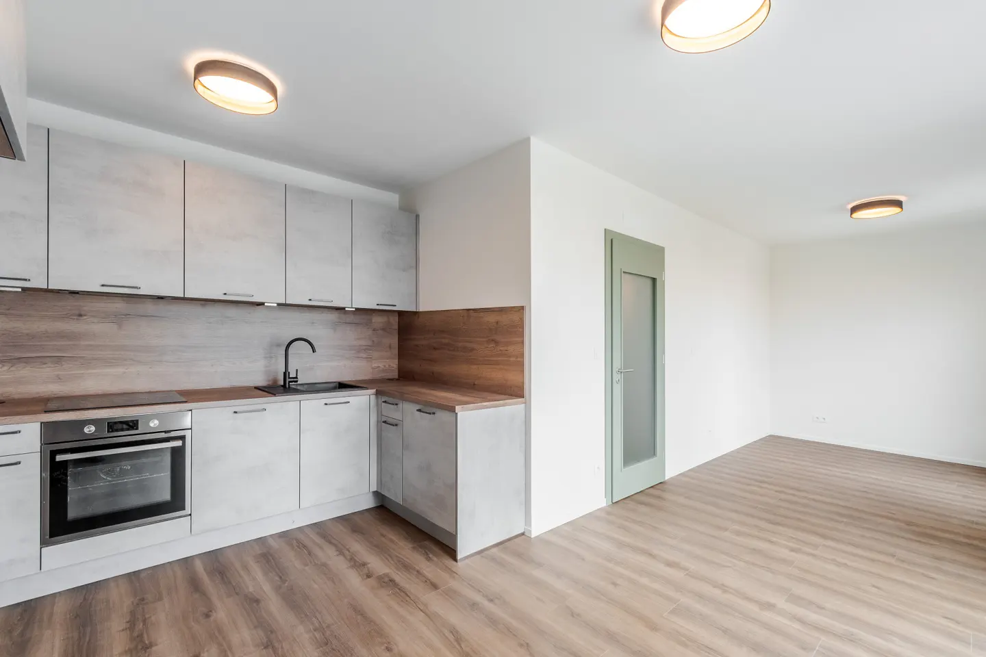 Modern kitchen with light grey cabinets, wood-look countertops, black faucet, and an open-plan living area with wood floors.