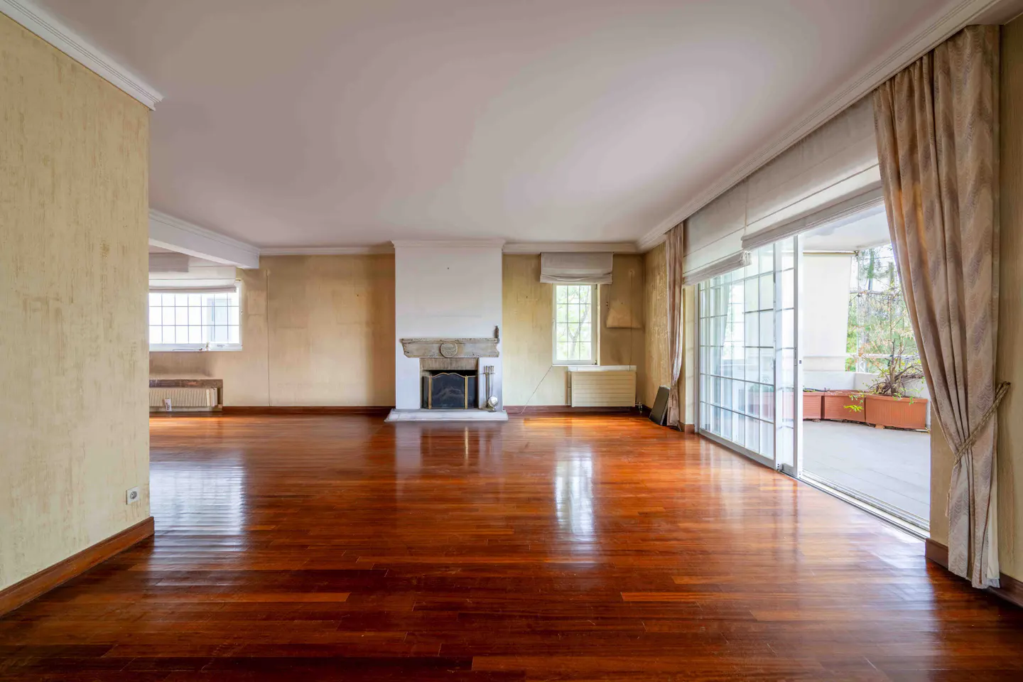 Spacious living room with polished hardwood floors, a central stone fireplace, beige walls, and sliding glass patio doors.