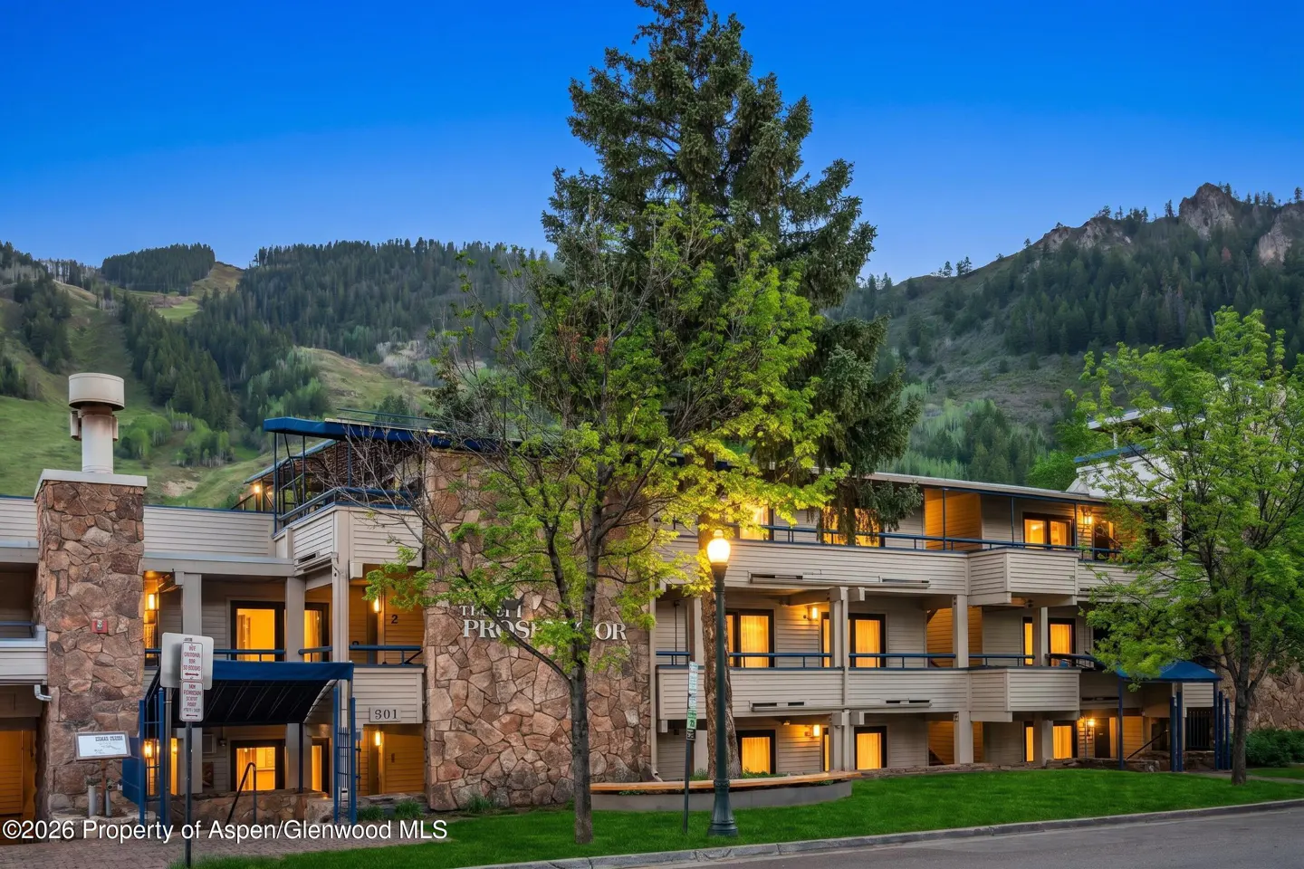 Exterior view of the Hotel Prospector, a multi-story building with stone accents and lit windows, set against a mountain backdrop.