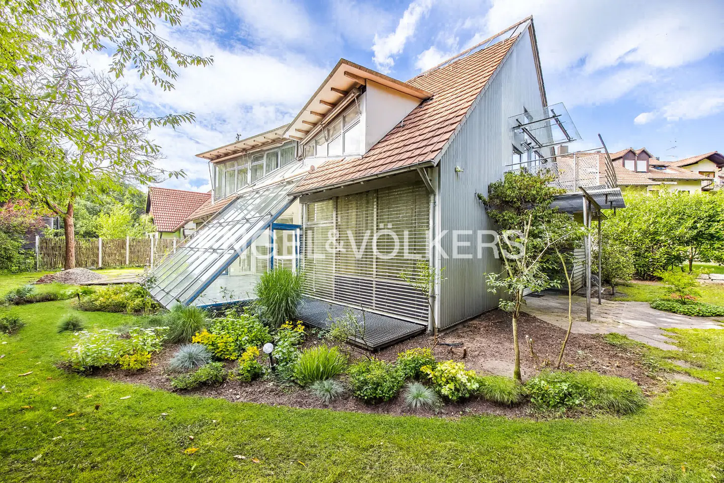 Exterior view of a modern house with a glass conservatory, a red-tiled roof, and a well-maintained green lawn.