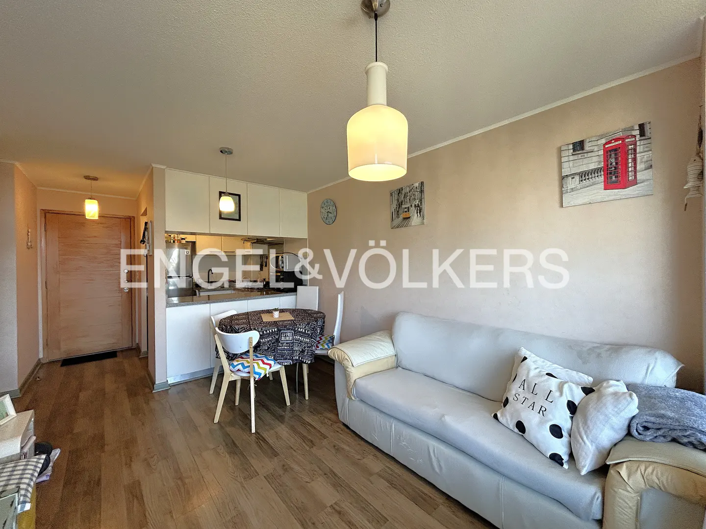 Living room with a white sofa, dining table, and open kitchen. Artwork of a red phone booth hangs on the wall.