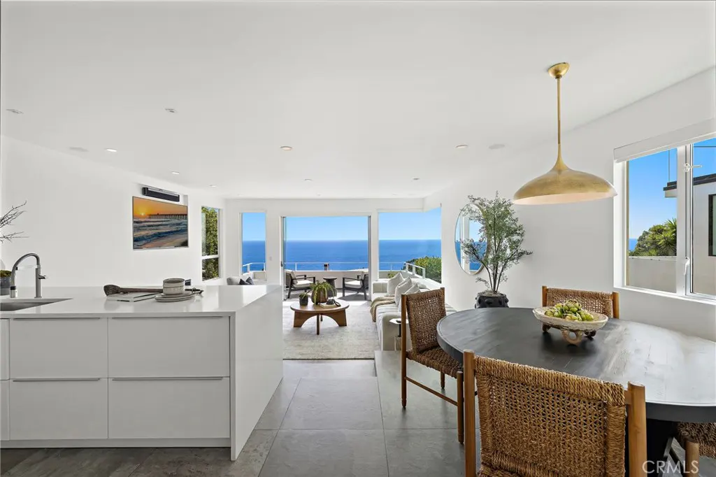 Modern open-concept living area with white kitchen island, dining table, and stunning panoramic ocean view from balcony.