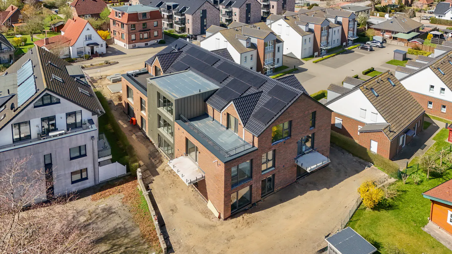 Aerial view of a modern brick house with solar panels, surrounded by other houses in a residential neighborhood.