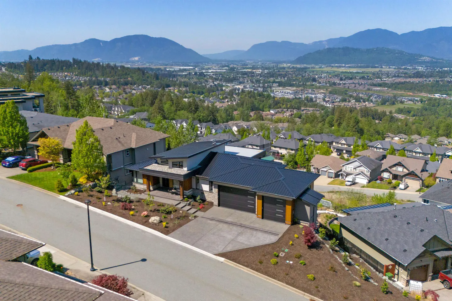 Aerial view of a modern two-story house with a dark roof, a two-car garage, and a mountain view.