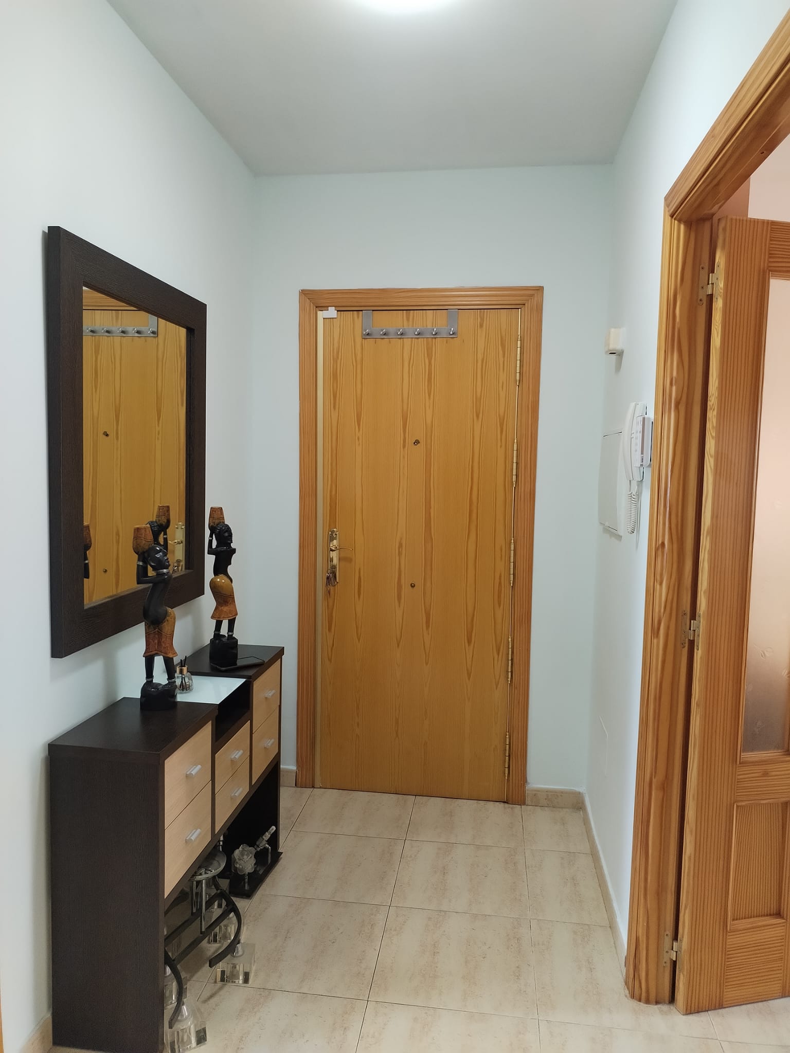 Entryway with light tile floors, a dark wood console table, a matching mirror, and a large wooden front door. [AI-generated text]