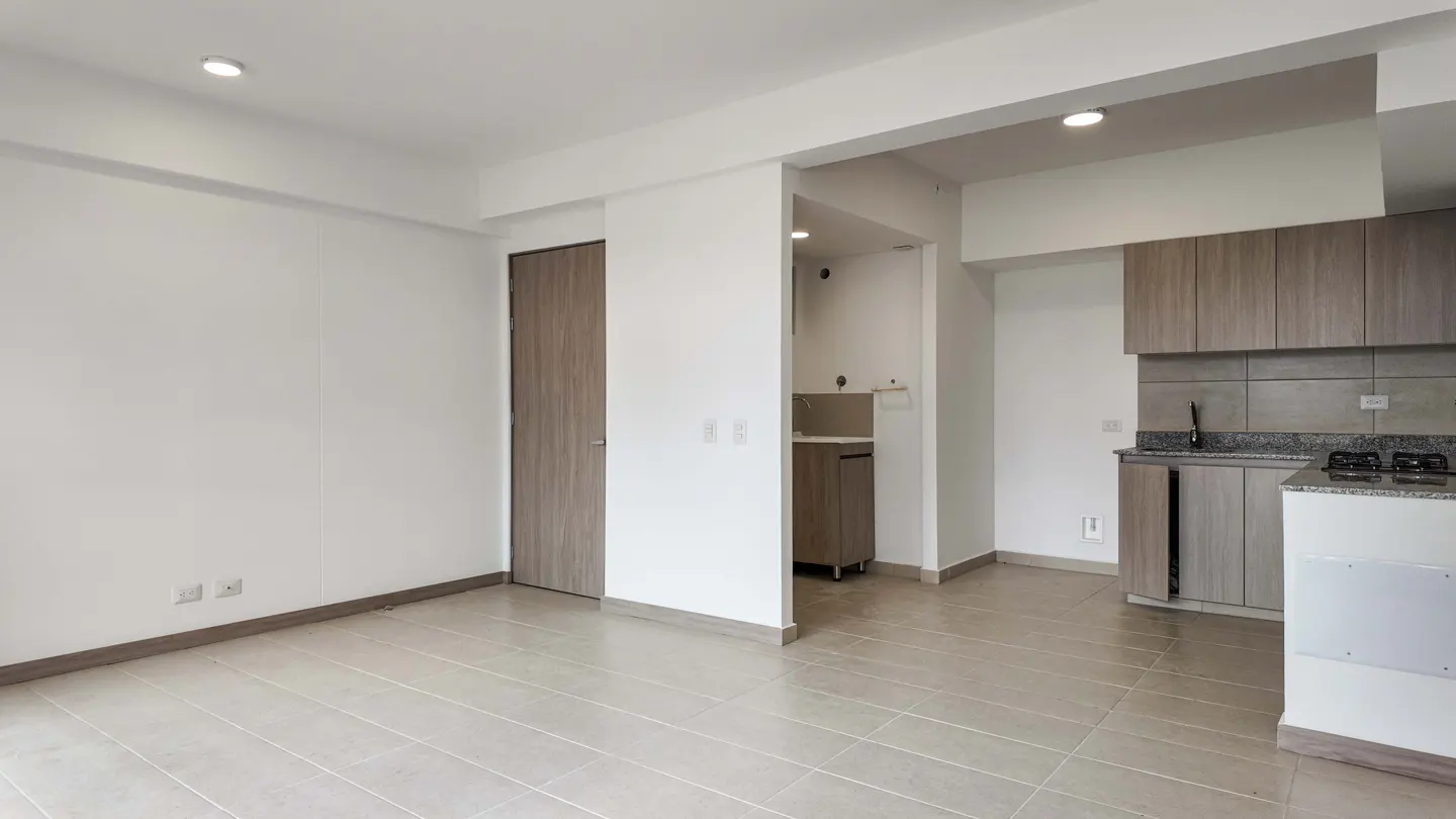 An empty, bright apartment with white walls, tile floors, and a modern kitchen with gray cabinets.