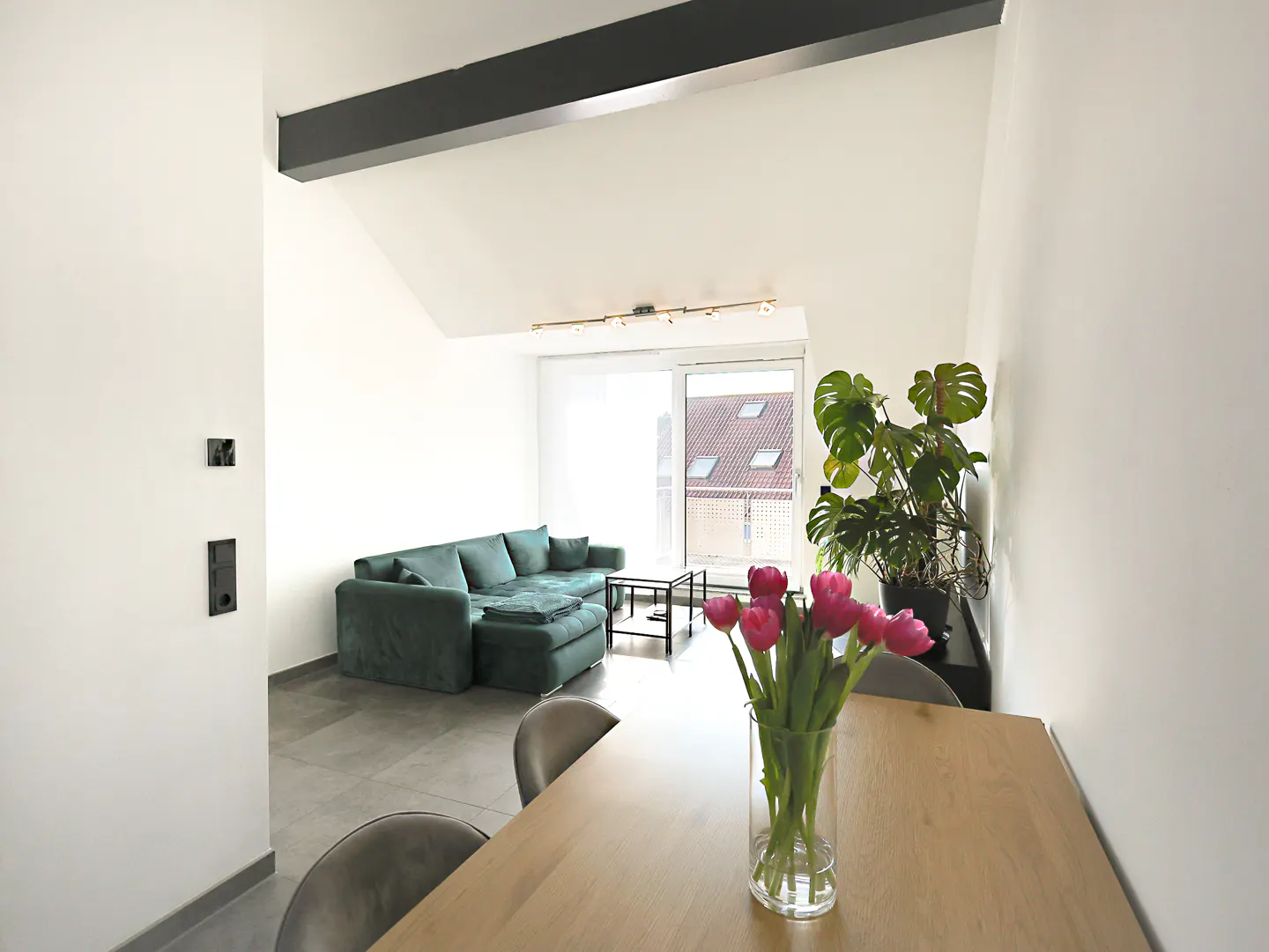 Bright living room with a green sofa, wood table with pink tulips, and a large monstera plant.