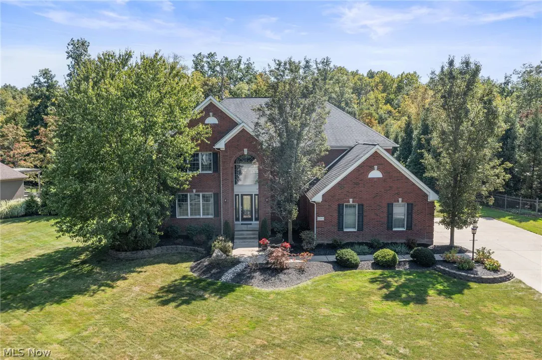 Two-story red brick house with a gray roof, green lawn, and trees in the background.
