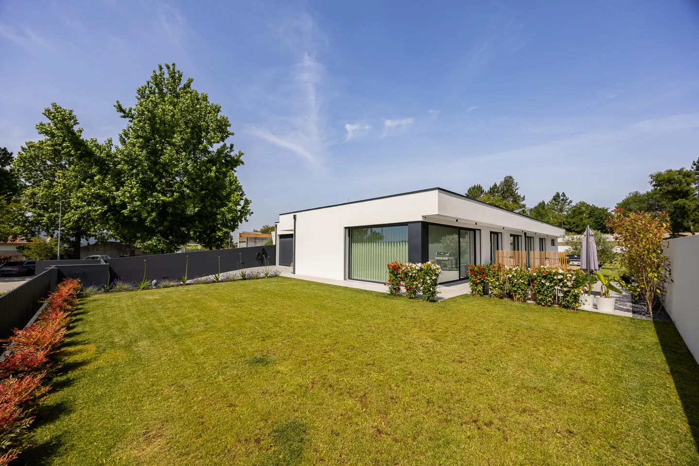 Modern white house with a green lawn, black trim, and large windows under a blue sky.