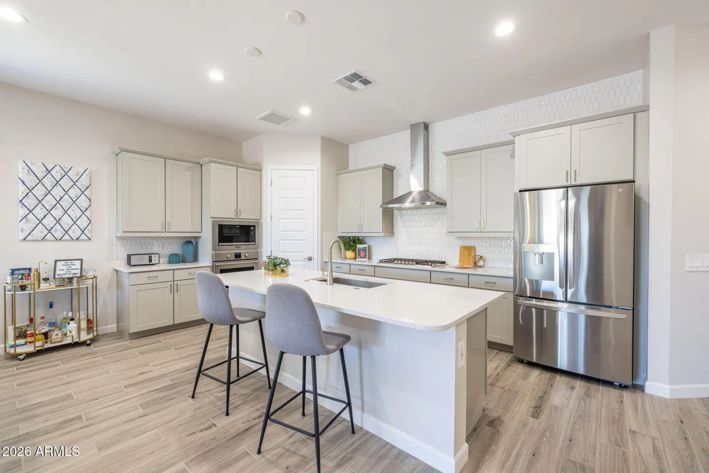 Bright kitchen with gray cabinets, stainless steel appliances, and a white countertop island with two gray chairs.