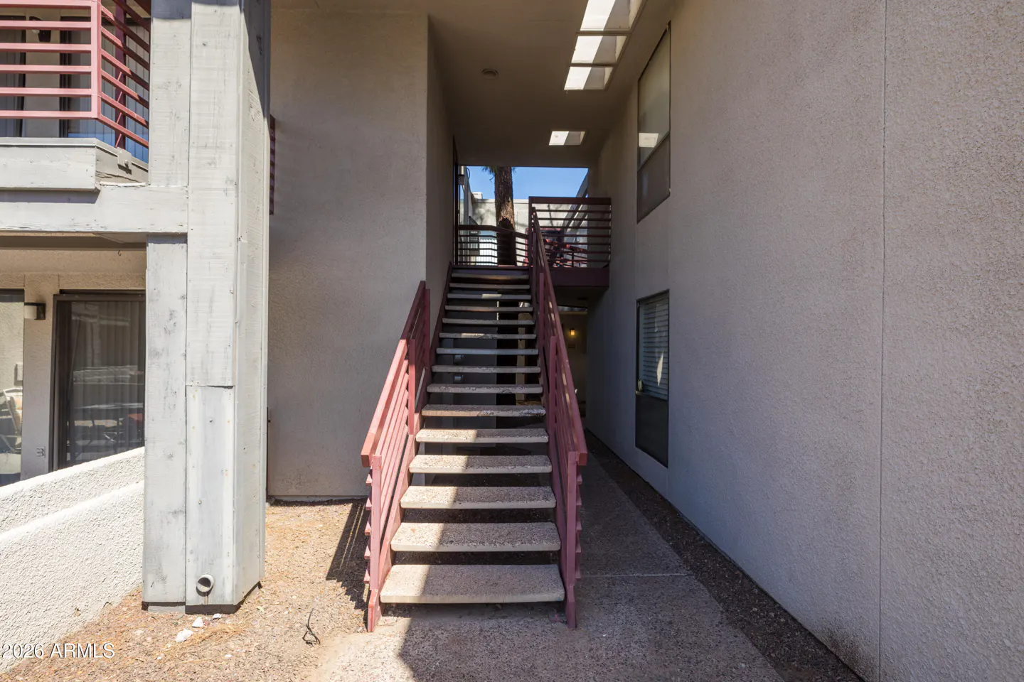 Exterior view of a building with a staircase. The stairs have pink railings and lead to an upper level. Windows are visible on the building's side.