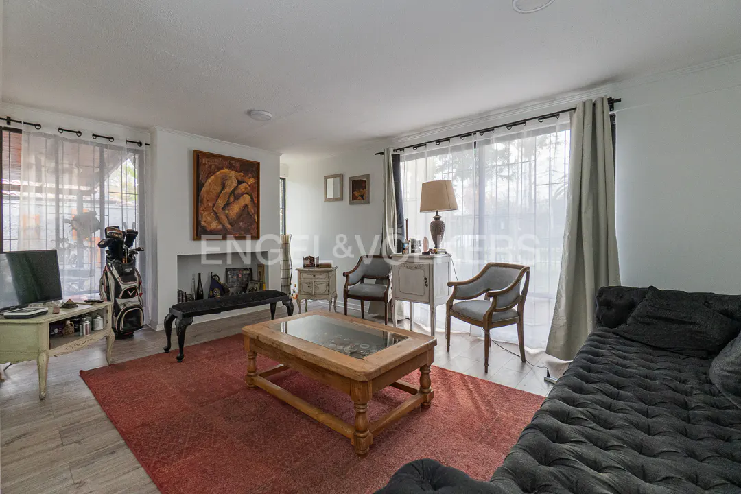 Living room with a dark tufted sofa, red area rug, wooden coffee table, two armchairs, and a fireplace with artwork above.