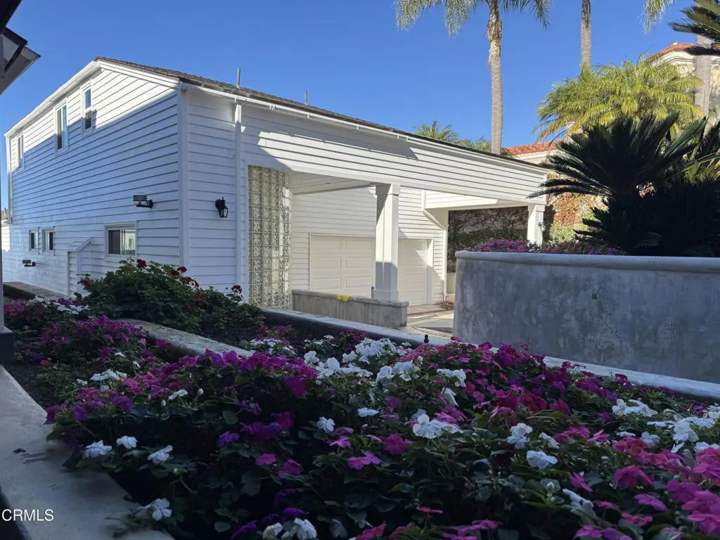 Two-story white house with a two-car garage and a flower bed with purple and white flowers in the foreground.