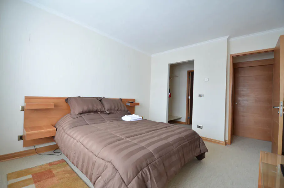 Bedroom with a brown striped comforter on the bed, a wooden headboard, and a beige carpet.