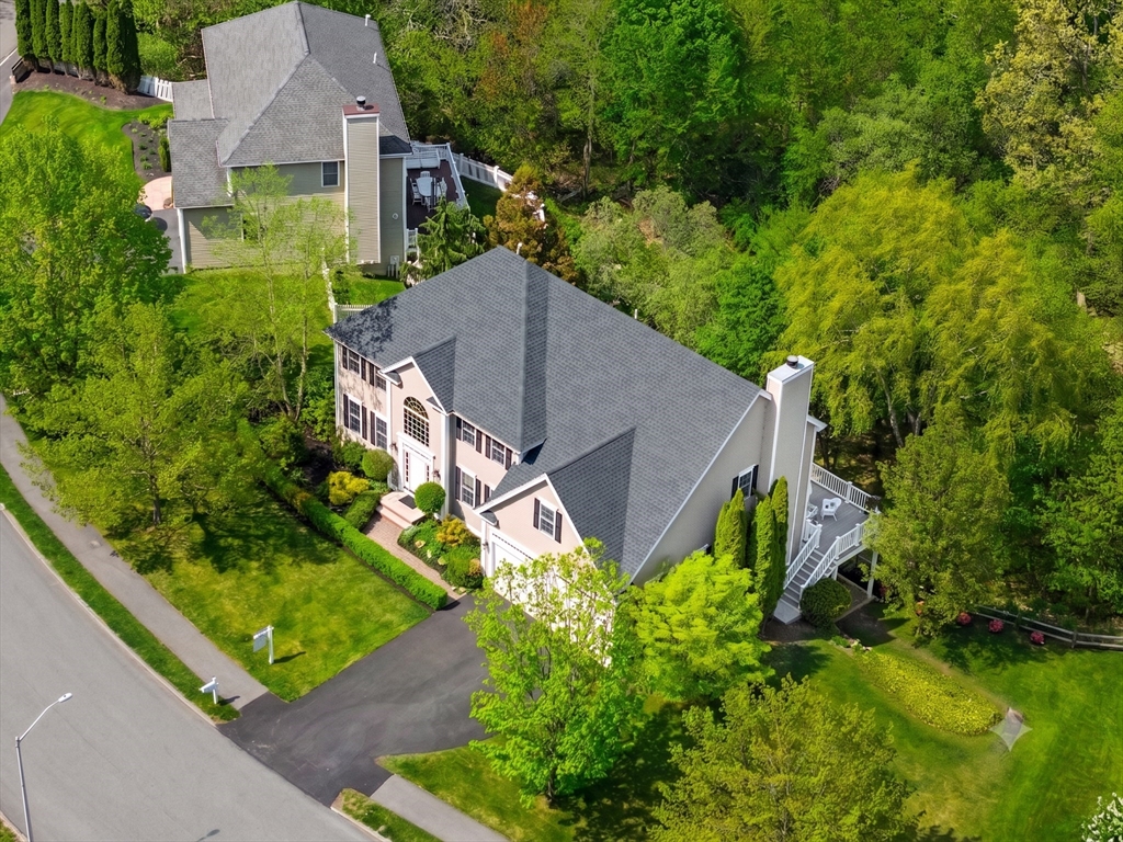 Aerial view of a two-story suburban home with a dark roof, light siding, and a deck, surrounded by lush green trees.