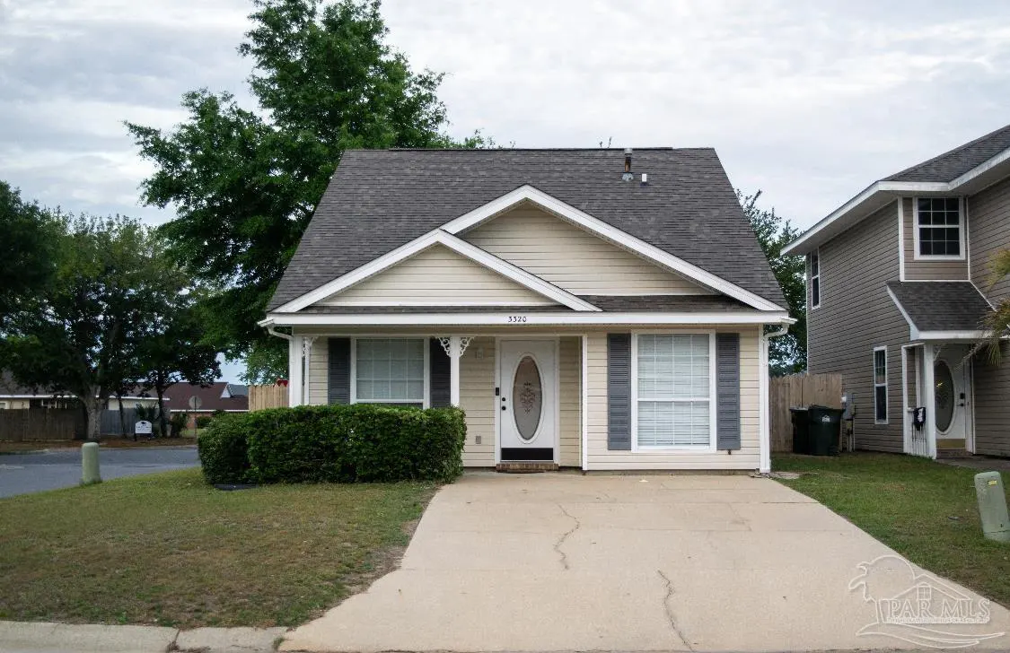 A beige single-story house with gray shutters and a gray roof, set on a green lawn with a concrete driveway.