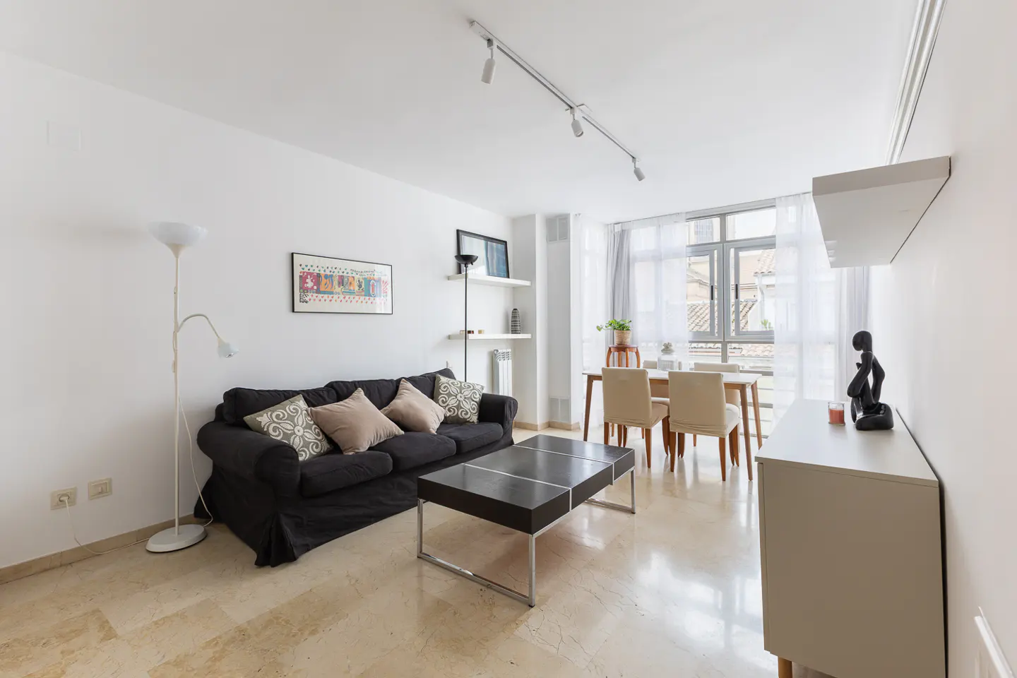 Bright living room with a black sofa, coffee table, dining table with chairs, and a white cabinet with a sculpture.