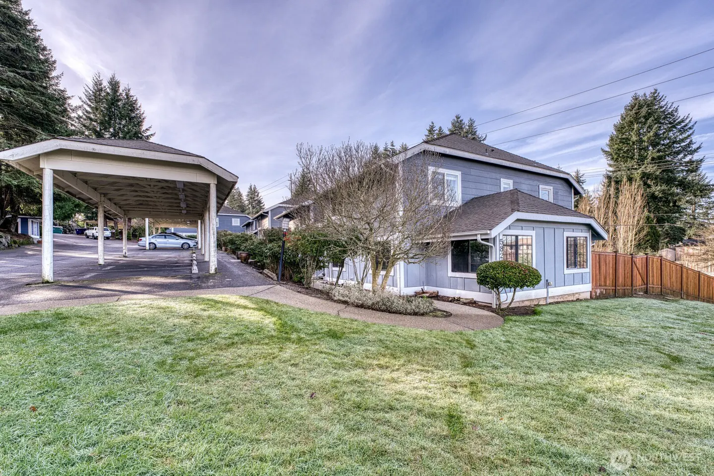 Exterior view of a two-story, light blue apartment building with a carport and green lawn.