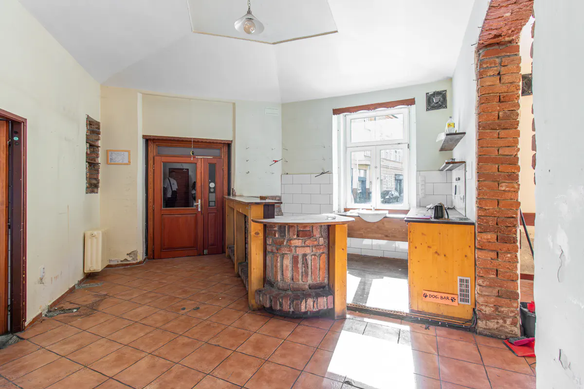 A kitchen with terracotta tile flooring, a brick archway, and a wooden bar with brick accents. A window provides natural light.