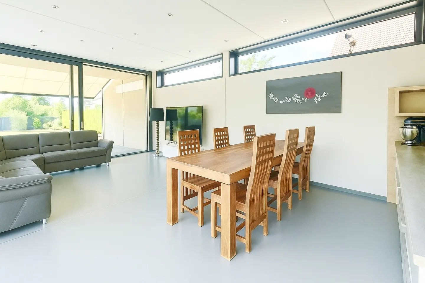 Bright, modern living room with a wooden dining table and gray sectional sofa near a large sliding glass door.