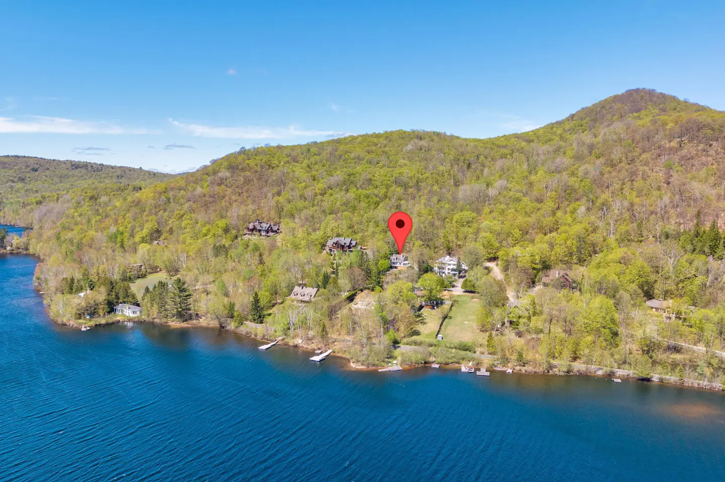 Aerial view of a lake house with a red pin, surrounded by green trees and blue water.