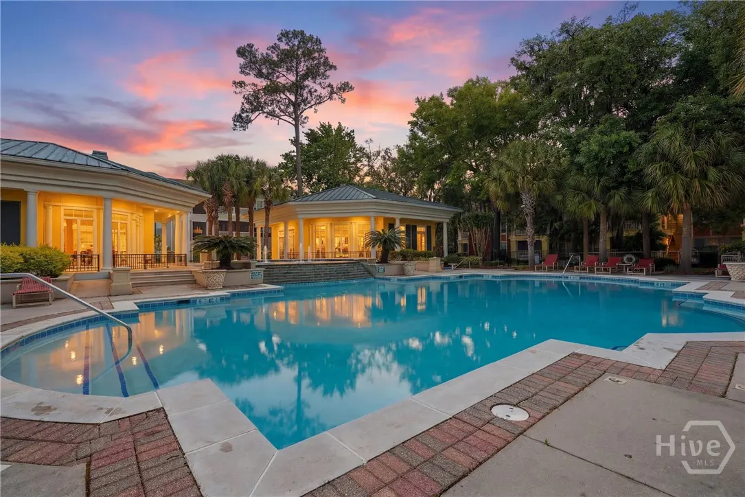 Outdoor pool with yellow buildings, palm trees, and lounge chairs at dusk. The sky is pink and blue.