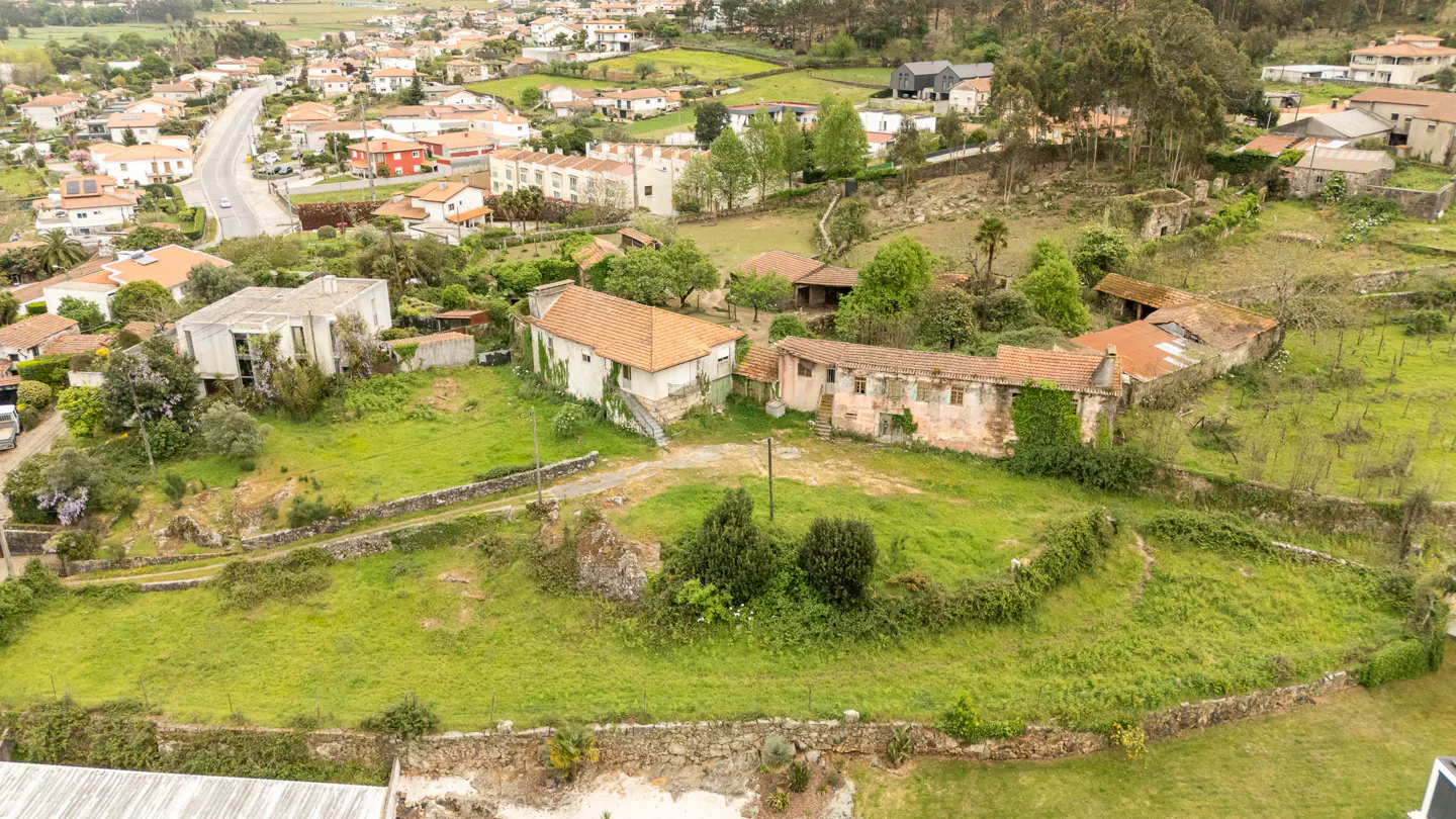 Aerial view of a rural landscape with houses, green fields, and trees. Some buildings appear old and in need of repair.