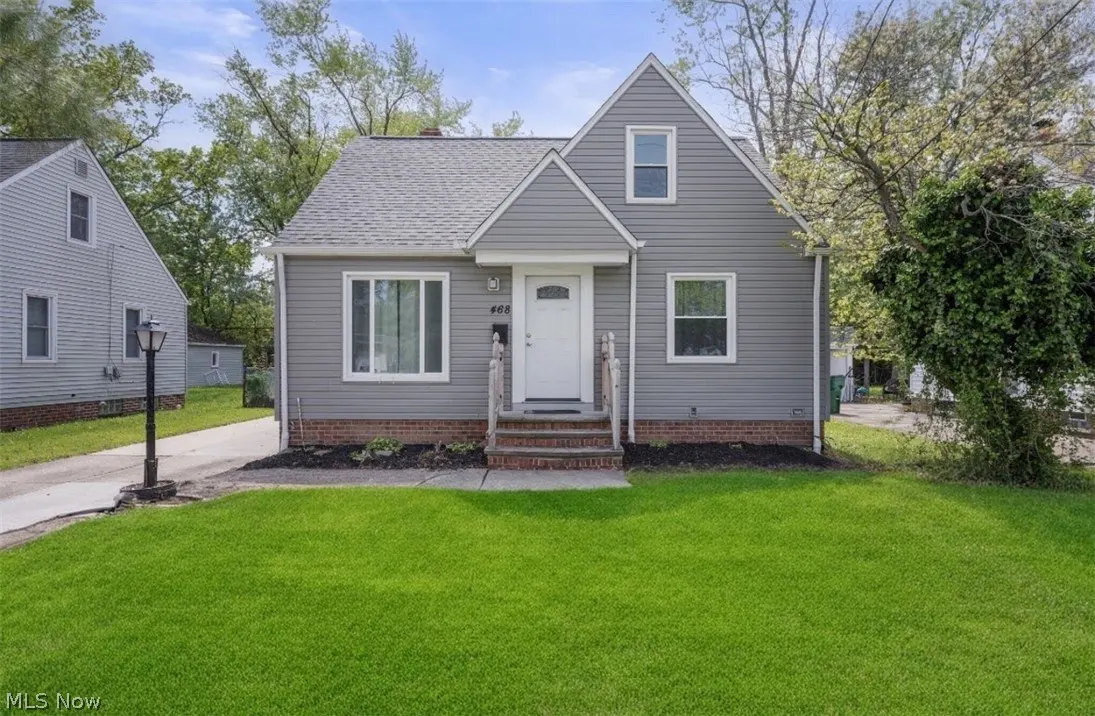 A gray, two-story house with a white door and green lawn on a sunny day.