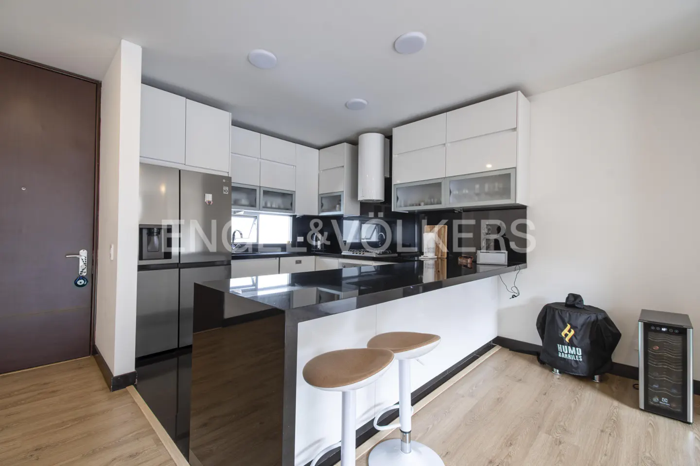 A modern kitchen with white cabinets, black countertops, stainless steel appliances, and two stools at the island.