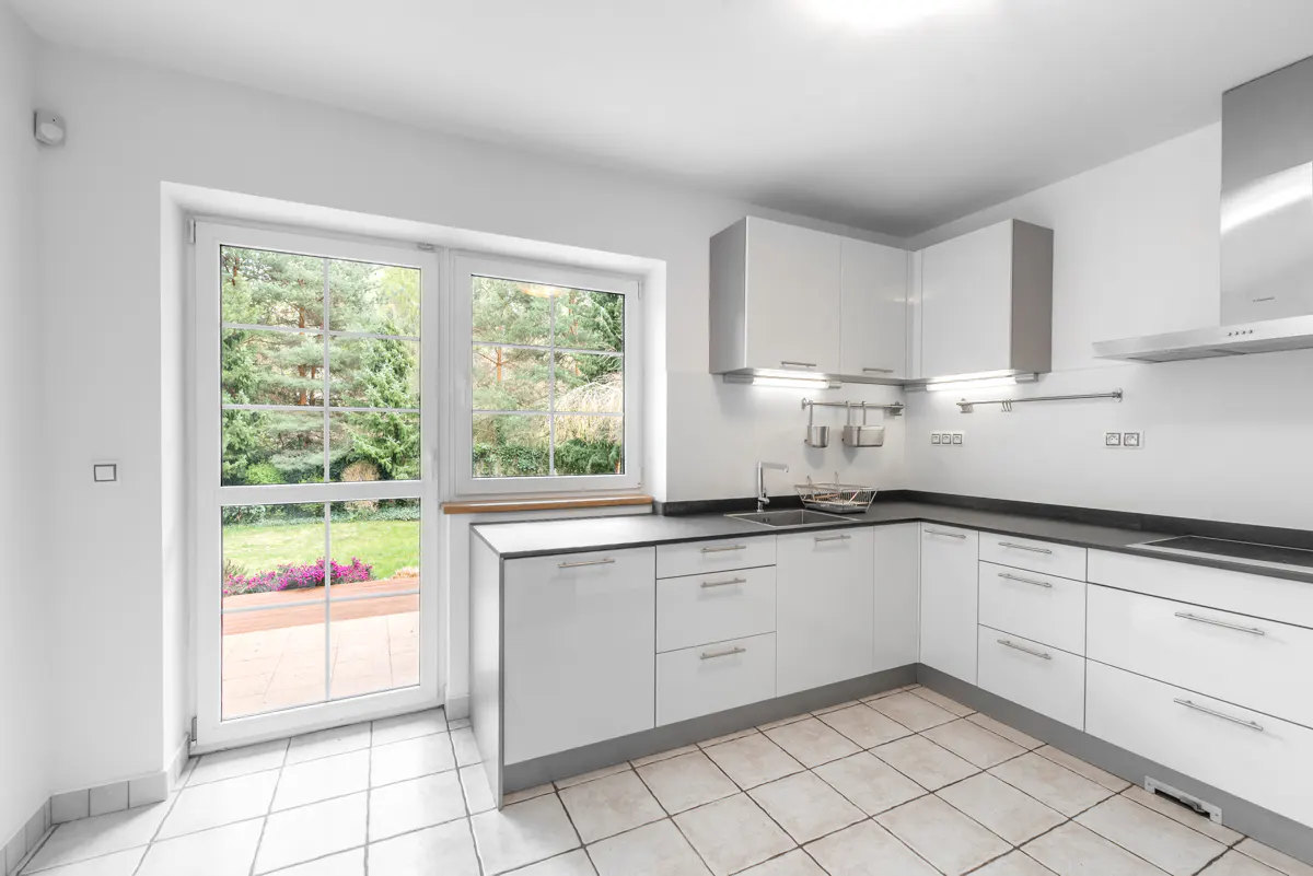 Bright, modern kitchen with white cabinets, black countertops, and tile floor. A window door looks out onto a green yard.