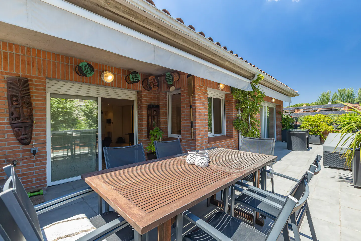 Spacious brick terrace with a wooden dining table, chairs, and decorative wall masks under a retractable awning.