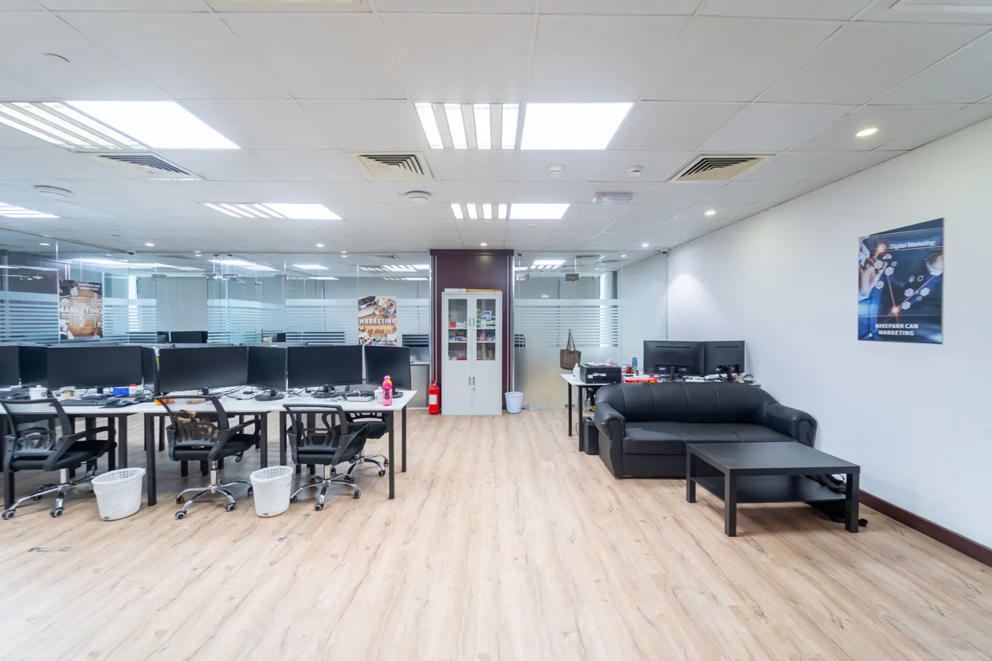 Bright, open office space with desks, computers, and a black sofa. Wood floors and white walls create a modern, professional atmosphere.