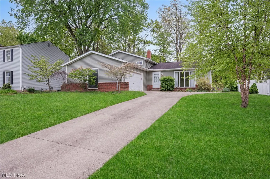 A single-story house with light green siding, a brick foundation, and a long concrete driveway.